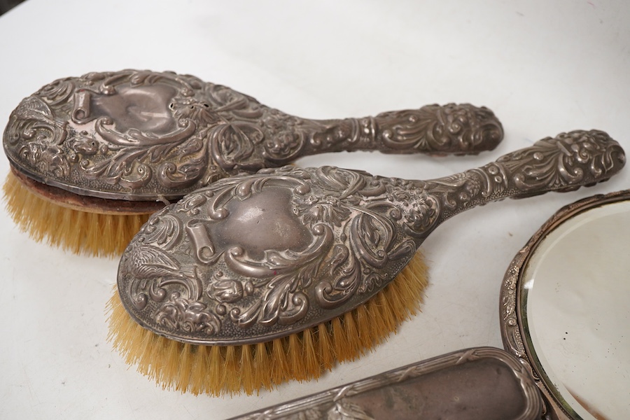 Four assorted early 20th century repousse silver mounted dressing table items to include a hand mirror, two hair brushes and a clothes brush(a.f.).